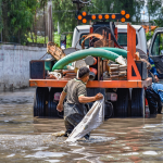 Trabalhadores caminham por áreas alagadas perto de um caminhão após fortes chuvas.