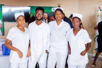 Quatro profissionais de saúde posam em ambiente interno, usando uniformes brancos.