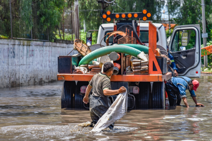 Trabalhadores caminham por áreas alagadas perto de um caminhão após fortes chuvas.