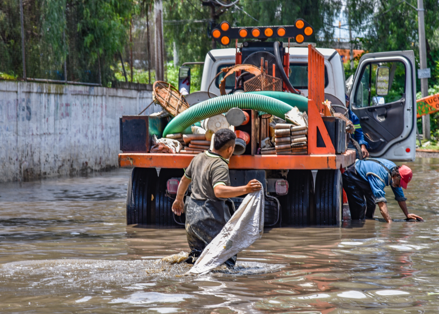 Trabalhadores caminham por áreas alagadas perto de um caminhão após fortes chuvas.