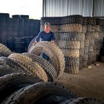 Trabalhador organiza pneus industriais empilhados em um armazém.
