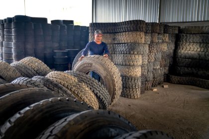 Trabalhador organiza pneus industriais empilhados em um armazém.
