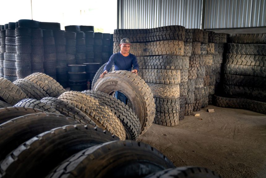 Trabalhador organiza pneus industriais empilhados em um armazém.