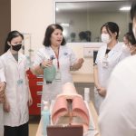 Grupo de estudantes de medicina pratica procedimentos em um manequim durante uma aula de treinamento.