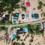 Vista aérea de casas alagadas em uma comunidade, com áreas inundadas ao redor das residências.