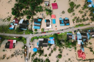 Vista aérea de casas alagadas em uma comunidade, com áreas inundadas ao redor das residências.