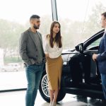 Casal conversa com um vendedor sobre a compra de um carro dentro de uma concessionária.