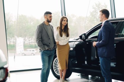 Casal conversa com um vendedor sobre a compra de um carro dentro de uma concessionária.