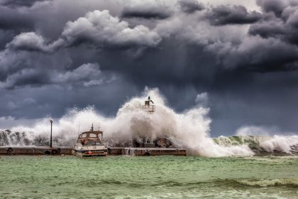 Ondas fortes quebram contra um píer e um farol sob um céu escuro e tempestuoso.